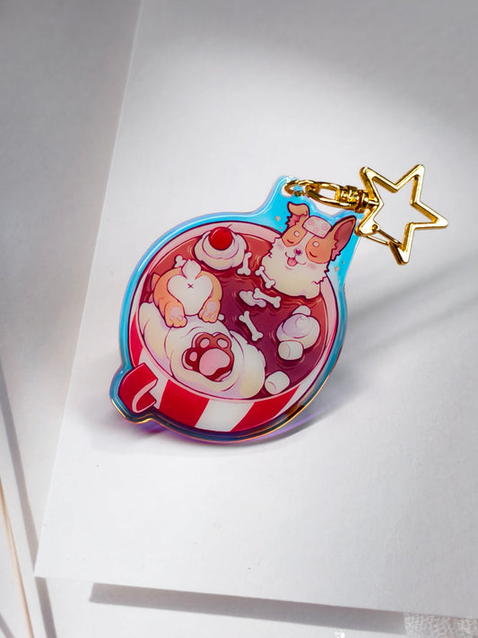 A colorful acrylic keychain charm shaped like a teacup with a cute character illustration, featuring a gold star keychain ring, resting on a white card.