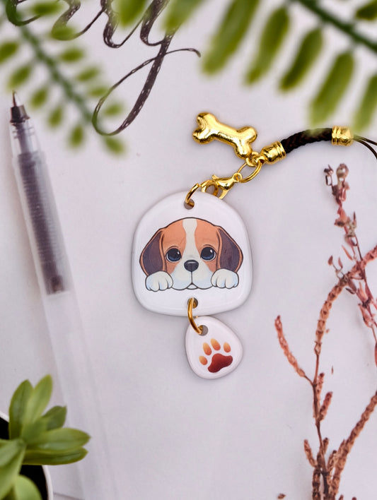 Beagle dog illustrated acrylic phone charm with a dangling paw print charm on a light surface with stationery.