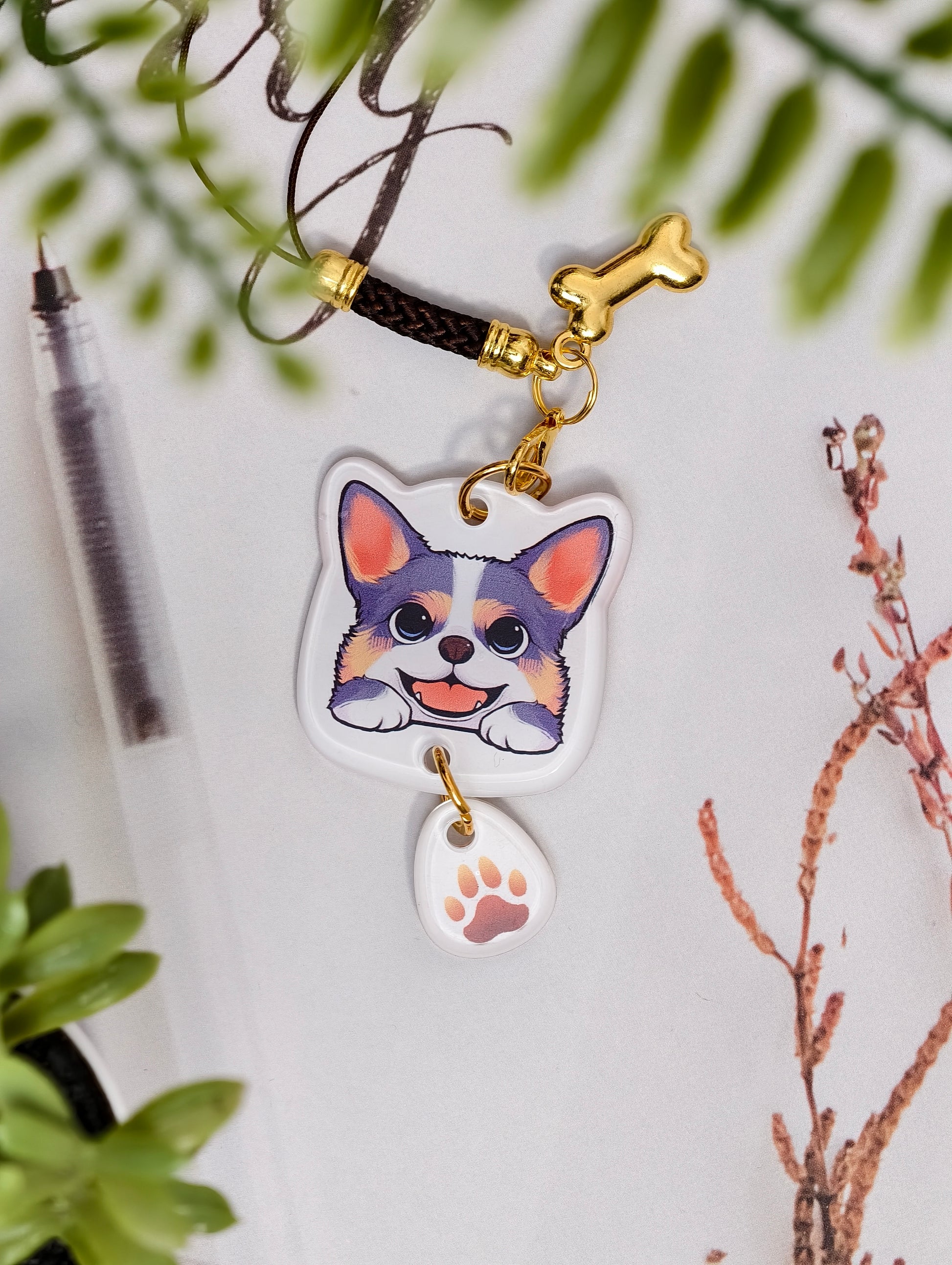 Corgi dog illustrated acrylic phone charm with a dangling paw print charm on a light surface with stationery.