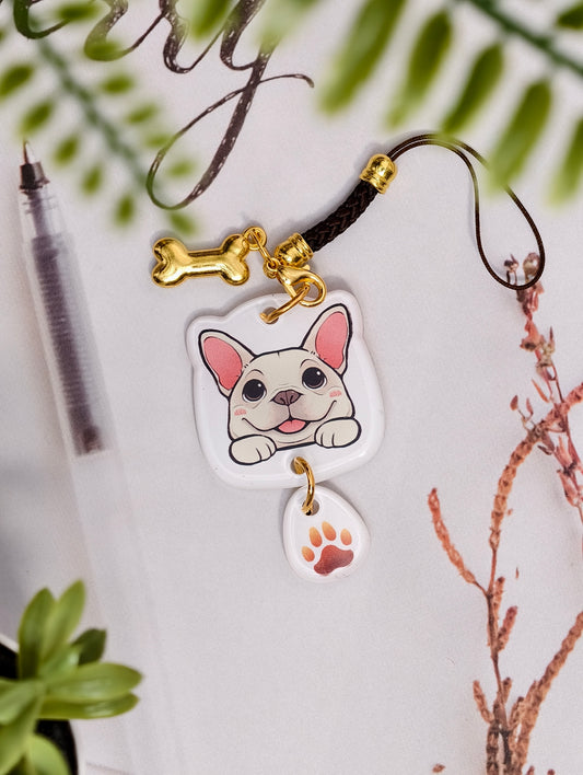 Frenchie dog illustrated acrylic phone charm with a dangling paw print charm on a light surface with stationery.