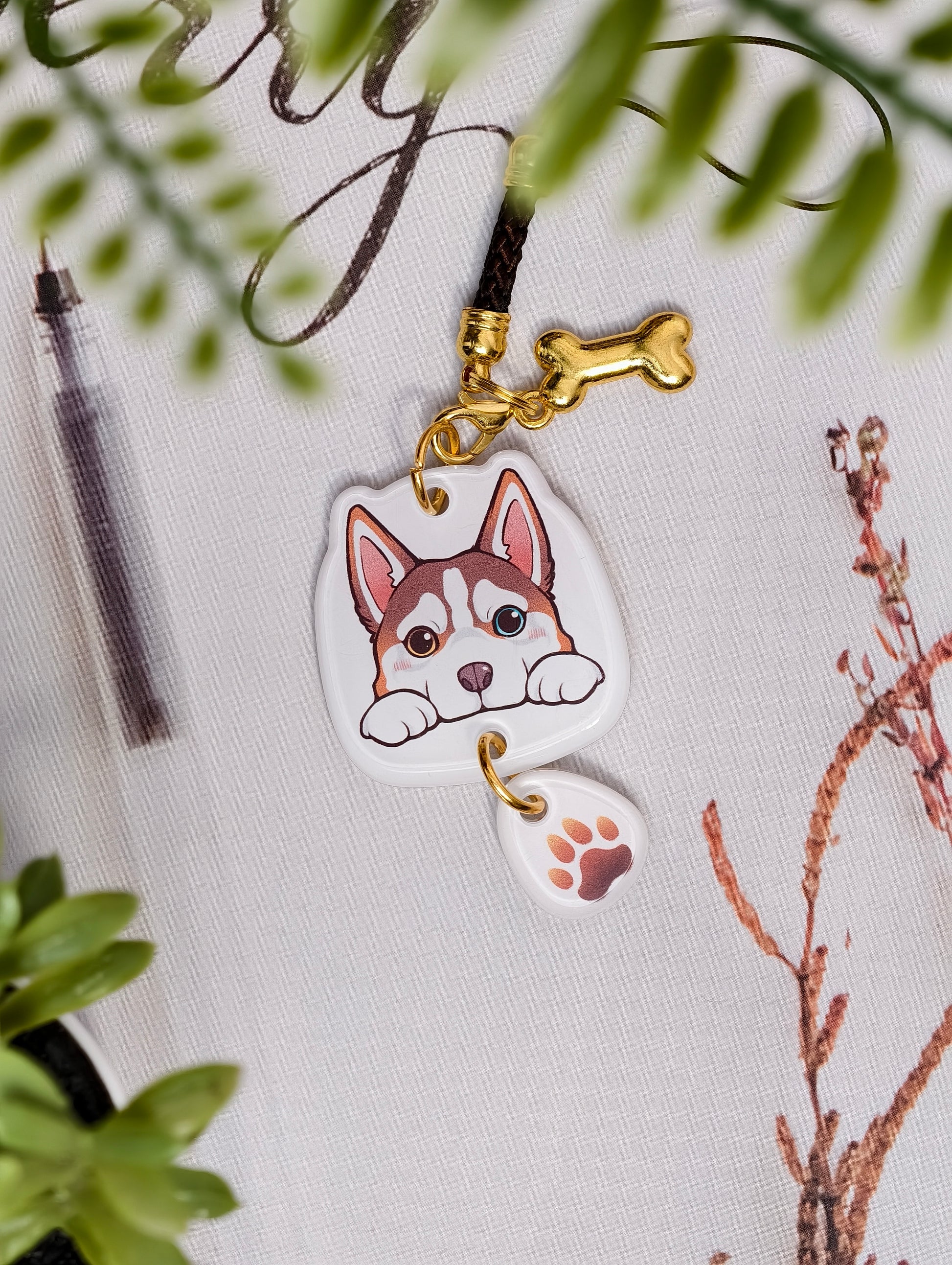 Husky dog illustrated acrylic phone charm with a dangling paw print charm on a light surface with stationery.