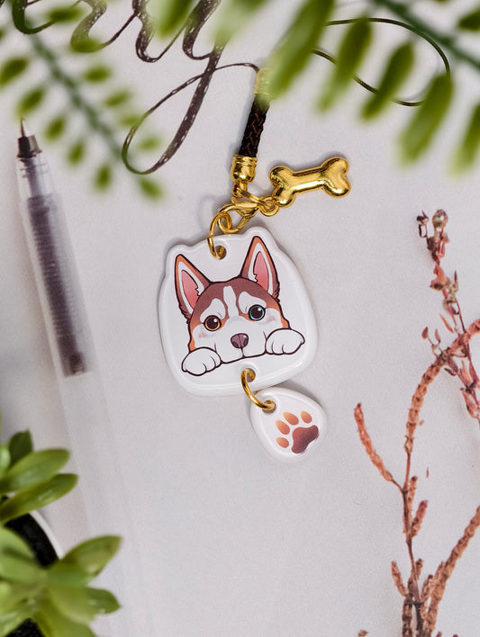 Husky dog illustrated acrylic phone charm with a dangling paw print charm on a light surface with stationery.