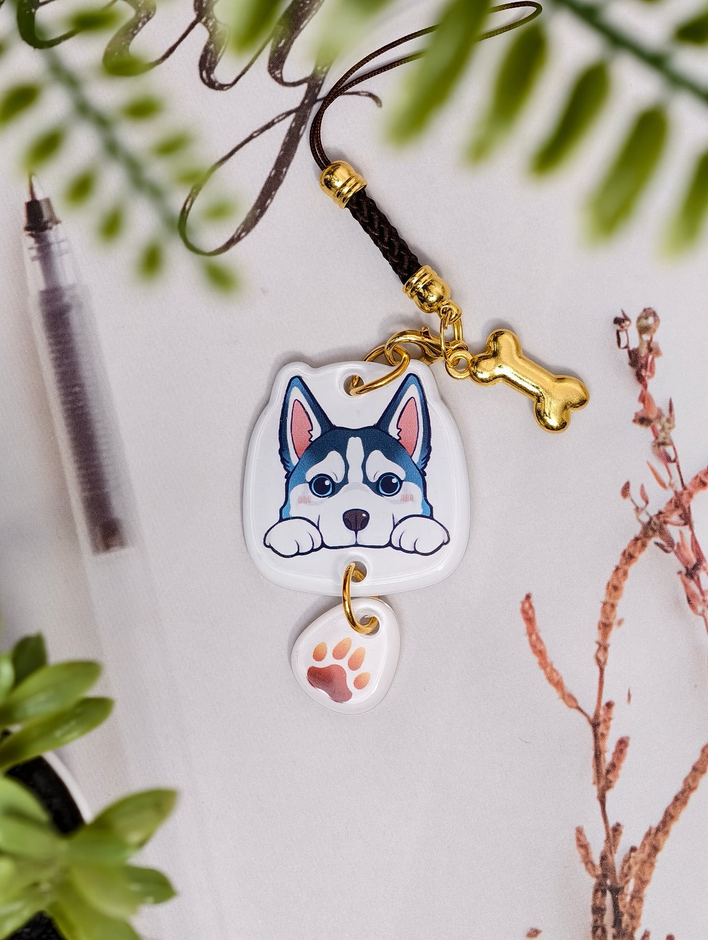 Husky dog illustrated acrylic phone charm with a dangling paw print charm on a light surface with stationery.