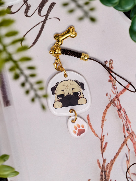 Pug dog illustrated acrylic phone charm with a dangling paw print charm on a light surface with stationery.