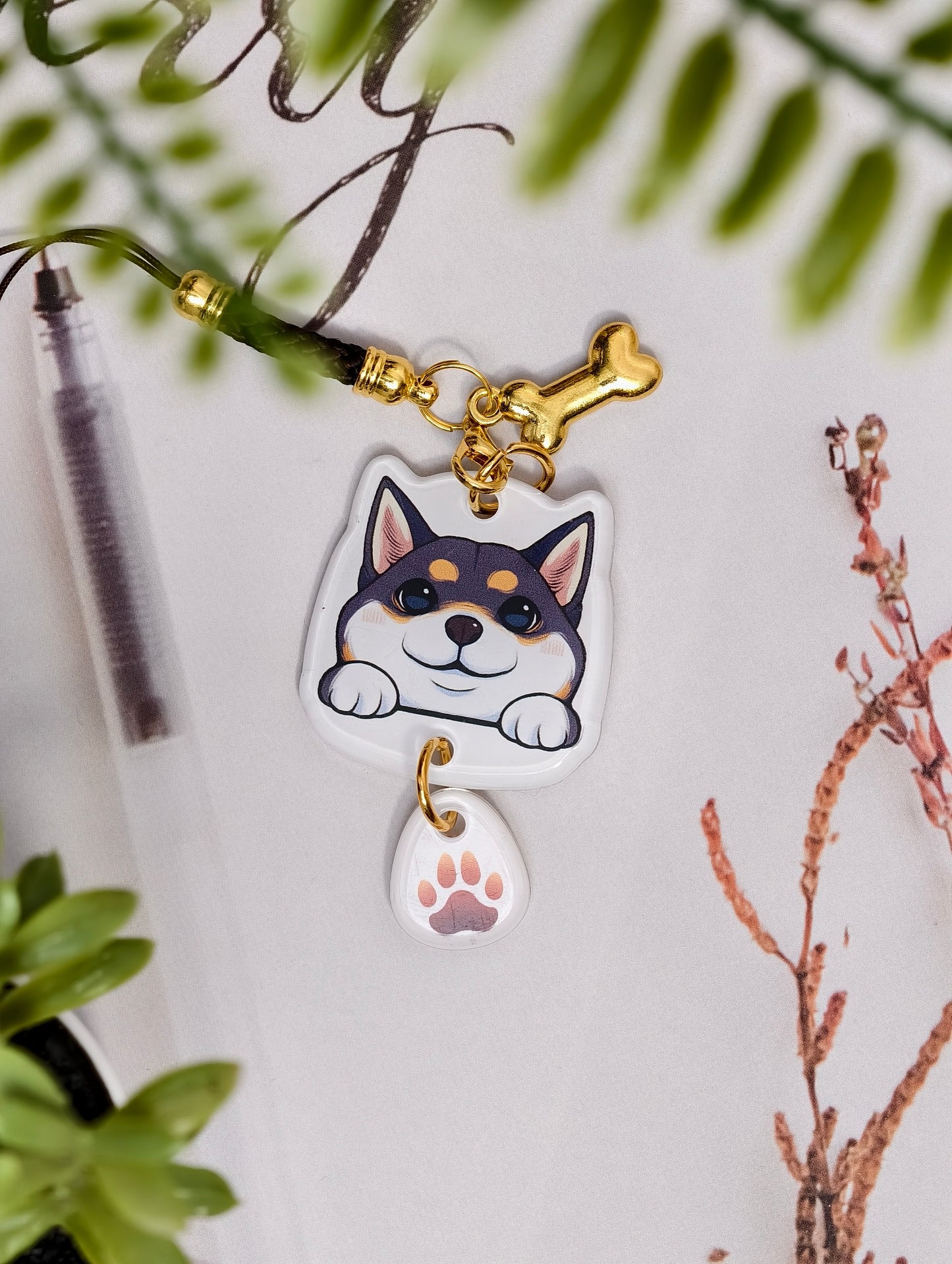 Shiba Inu dog illustrated acrylic phone charm with a dangling paw print charm on a light surface with stationery.